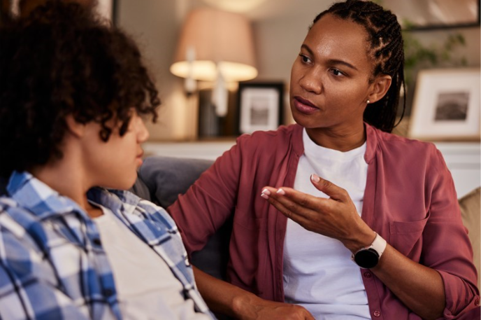 Adult woman talking with a child while sitting together on a couch, offering guidance and support during a conversation.